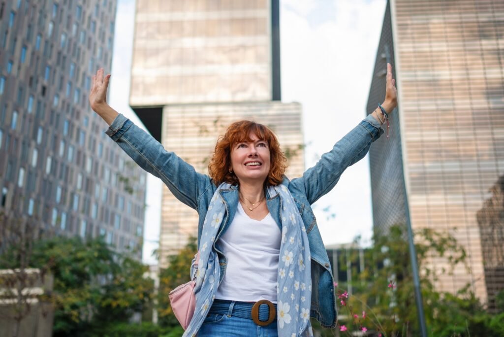 Happy senior businesswoman raising arms in modern business district celebrating success